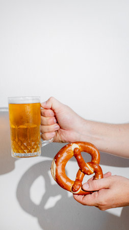 Close up of person holding a beer and pretzel, celebrating Oktoberfest, emphasizing traditional...