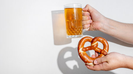 Hands holding a beer mug and pretzel, symbolizing Oktoberfest and German cultural festivities