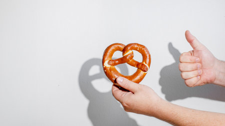 A hand giving a thumbs up while holding a pretzel, symbolizing enjoyment of Oktoberfest traditions and festive snacksの写真素材