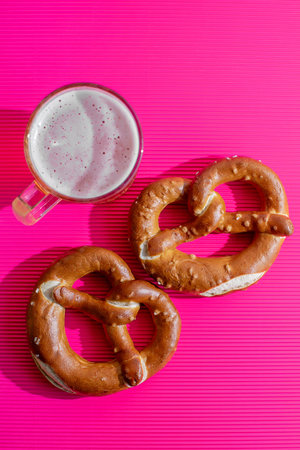 A mug of beer with two soft pretzels on a vibrant pink background, related to Oktoberfest...