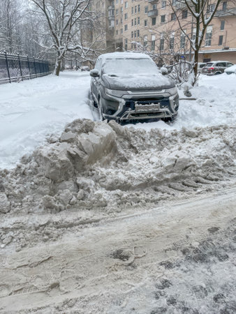 A snow covered SUV is parked near an apartment building, illustrating winter weather challenges and urban snow removal issuesの写真素材