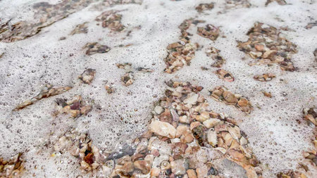 Waves gently wash over a pebbled beach, creating a serene natural texture ideal for environmental...