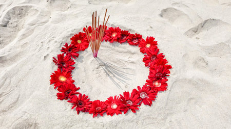 A circle of red flowers and incense sticks on sand symbolizes the Thai holiday Loy Krathongs spirit of remembranceの写真素材