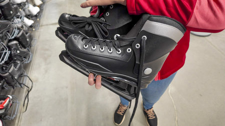A person in a red jacket holds new black ice skates in a store, illustrating winter sports shopping
