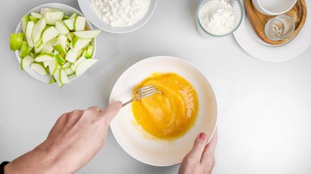 A person prepares apple pancake batter by mixing eggs, flour, and sliced green apples, perfect for a...