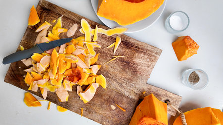 Fresh pumpkin being peeled on a wooden cutting board, ideal for autumn recipes or preparing for Thanksgiving mealsの写真素材
