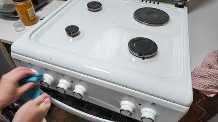 Hands cleaning a white gas stove in a kitchen setting, emphasizing hygiene and home maintenance before Thanksgivingの写真素材