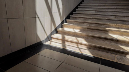 Sunlight casts geometric shadows on a modern indoor staircase, symbolizing architectural design and tranquilityの写真素材