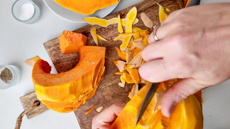 A close up of hands peeling pumpkin on a wooden board, symbolizing autumn harvest preparation and Halloween cooking traditionsの写真素材
