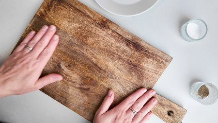 Hands placing a wooden cutting board on a table with spices, symbolizing kitchen preparation for a meal, Caucasian ethnicityの写真素材