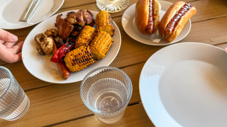 Summertime feast with grilled maize and sizzling sausages, echoing backyard juneteenth celebrations and outdoor picnics, multicultural flavors uniteの写真素材