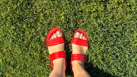 Vibrant red sandals on verdant grass, evoking Midsummer revelry, barefoot grounding, nostalgic childhood playgrounds, female, carefree spiritの写真素材