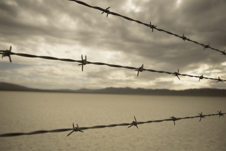 Barbed wire against cloudy sky over desert landscape in Nevada. Selective focus on barbed wire.の写真素材