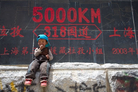 CHINA, TIBET, APRIL 18: A dreamy unidentified Kid in front of a roadsign.The Signs tell that we are exactly 5000 Km from Shanghai, on the Friendship Highway In Tibet, 18 April 2013.のeditorial素材