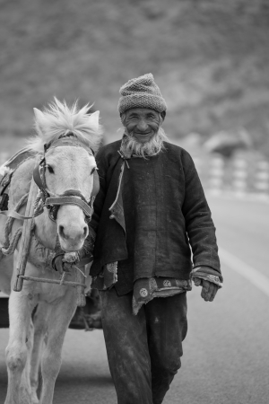 CHINA, TIBET, APRIL 17  A very expressive unidentified farmer with his beautifull white horse on the road to of Friendship Road towards Kathmandu , 17 April 2013 のeditorial素材
