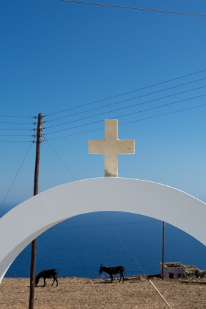 Orthodox Cross and donkeys eating in front of the Aegan sea.The cross is from the roof of Agios Ioanis Prodromos Church, Ano Mera, Pano Meria Village, Folegandros, Cyclades Islands. These churches are scattered across the tiny island, often in incredibly の写真素材