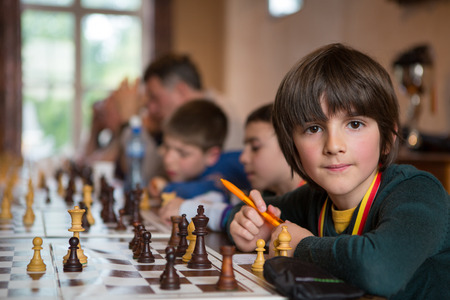 BRUSSELS, BELGIUM, JUNE 26: Serious little boy playing chess holding a pen and looking at the camera while other students are learning chess in the background with a teacher. Brussels 2013のeditorial素材