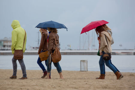 Unrecognizable group of women walking on the beach and holding umbrellas during a rainy day in Sopot...