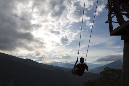Silhouette of happy young man on a swing with a fantastic mountain view at the Casa del Arbol,...