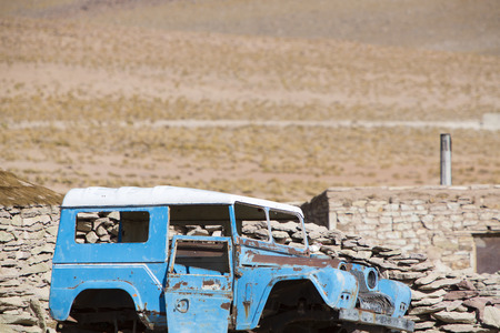 Rusted blue off-road old car left in a remote village with house made of stones in the background. Boliviaの写真素材