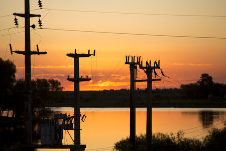 Beautiful, dramatic, colorful clouds and sky at sunset. Silhouettes of electrical wires and stakes and water reflexions.の写真素材