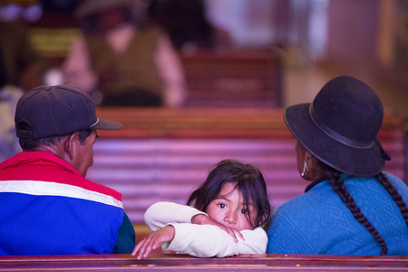 TUPIZA, BOLIVIA, DECEMBER 28: Young Bolivian girl sitting with her parents at the church and looking behind her at the camera. Tupiza - Bolivia 2014. (image with grain)のeditorial素材