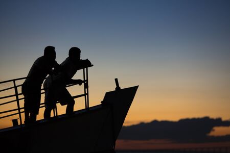 Sunset and silhouettes of two men standing on a boat and cruising on the Amazon River, clear blue orange sky. Manaus, Brazil 2015の写真素材
