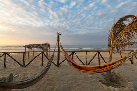 View of cozy straw hammocks on a tropical white beach with sunset light, Punta Sal near Mancora in Peru.の写真素材