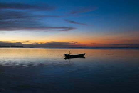 Amazing blue orange sunset with silhouette of anchored small wooden fisher boat with still ocean on...