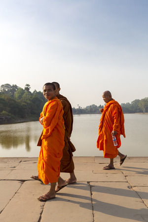 Three smiling Cambodian monks dressed in orange and walking Toward Angkor Wat temple with the pond in the background. UNESCO heritage site, Cambodia 2016のeditorial素材
