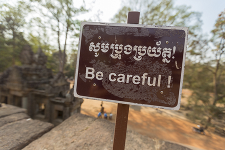 Be careful warning sign at at Ta Keo temple near Angkor Wat with entrance of the temple in the background, Unesco Heritage site in Cambodia. Selective focus.の写真素材