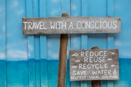 Wooden sign saying to travel with a conscious wooden on blue  wall background.の写真素材