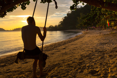 Silhouette of man swinging on tropical paradise beach at sunset, happy people enjoying summer. Koh Chang island, Thailand 2016の写真素材