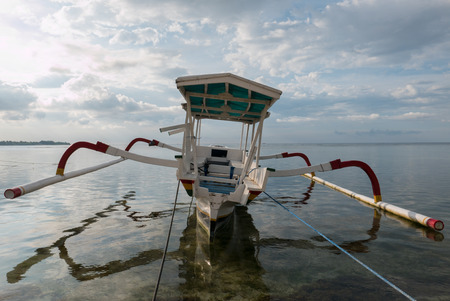Rear view of traditional Indonesian fisher standing on the beach boat at beautiful Gili Air Island beach in Lombok, Indonesia.の写真素材