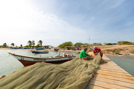 Two Venezuelan fishermen working on a wooden pier to fix Their fishing net with the beach in the...
