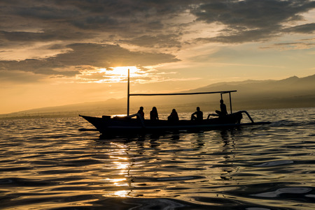 Silhouette of traditional small wooden boat with people on board on calm ocean with reflection in the water in Lovina, Bali. Indonesia 2016. Serene scene landscape.の写真素材
