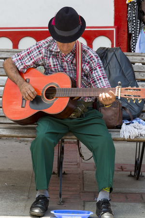Portrait of old Colombian musician playing guitar in the touristic street of Salento with colored traditional architecture in the background. Colombia 2015のeditorial素材