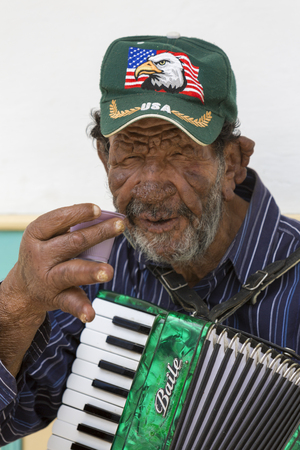 Old Colombian musician playing accordion in the touristic street of Salento with colored traditional architecture in the background. Colombia 2015のeditorial素材