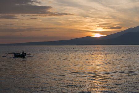 Amazing romantic orange sunset with silhouette of fisher man fishing on his small wooden fisher boat near Gili Air Island, Lombok. Indonesiaの写真素材