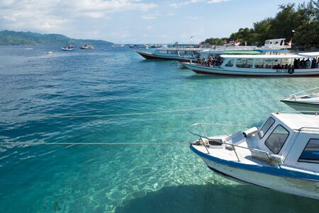 Harbor of Trawangan Island with boats moored small, tourists and turquoise sea water of Gili...
