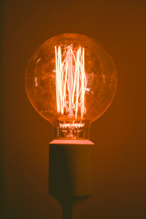 A glowing vintage-style lightbulb with visible filaments sits on a simple base.の写真素材