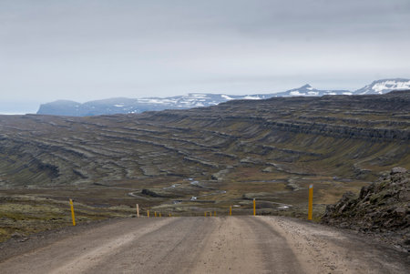 A gravel road leads to a valley with layered hills and snow-capped mountains.の写真素材