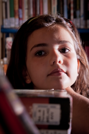A little girl looking for a book in the library shelvesの写真素材