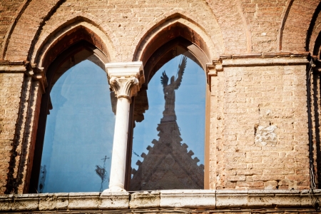 The window of a medieval palace in Siena  Santa Maria della Scala  opposite the cathedral, with the stature of an angel reflected on the glass の写真素材