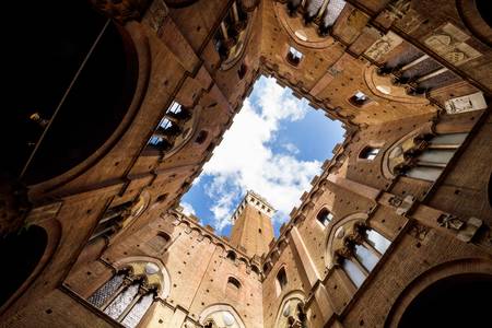 View of the tower of the city hall in Siena (Torre del Mangia) from inside the palace yard (Cortile del PodestÃ ).の写真素材