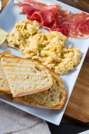 A plate with scrambled eggs with ham and toasted bread. Delicious breakfast.の写真素材