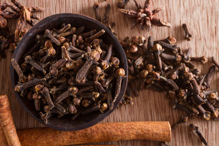 Spices series: a bowl full of cloves against a wooden background. Copy space. Star anise and...
