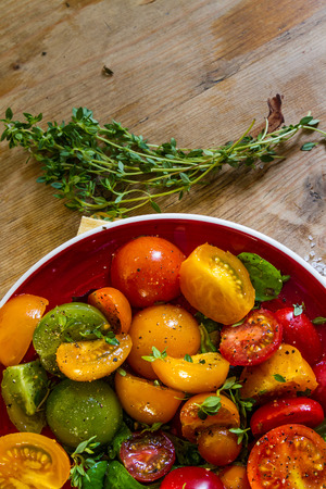 Yellow, red, green, orange tomatoes with olive oil, pepper, rock salt and sprigs of thyme on a red dishの写真素材