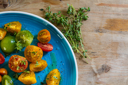 Yellow, red, green, orange tomatoes with olive oil, pepper, rock salt and sprigs of thyme on a bright blue dishの写真素材