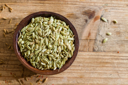 Fennel seeds in a small wooden bowl on an old wooden table.の写真素材